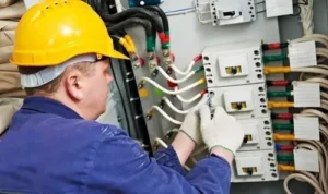 commercial electrician wearing a yellow hard hat repairing an industrial electrical panel