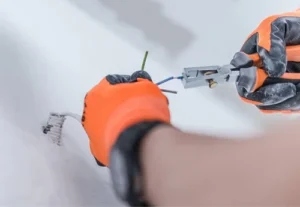 a close up of an electrician wearing orange safety gloves installing new electrical wiring within a wall